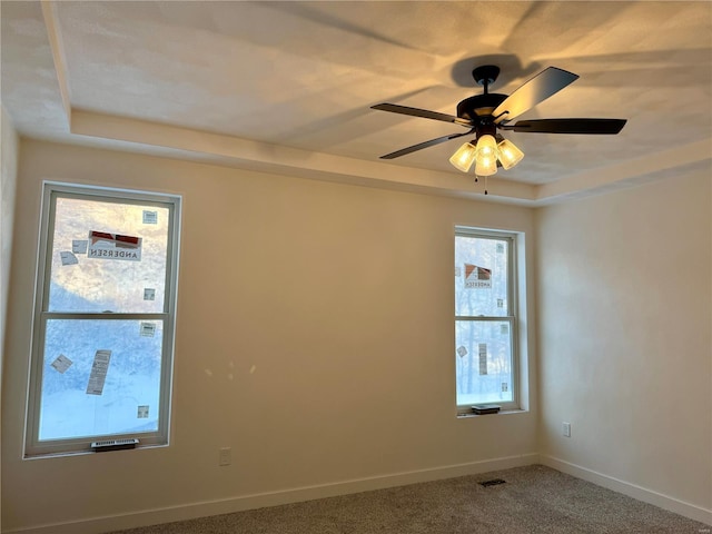 empty room featuring carpet, ceiling fan, a healthy amount of sunlight, and a tray ceiling