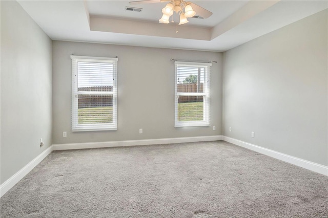 empty room with carpet flooring, a raised ceiling, and ceiling fan