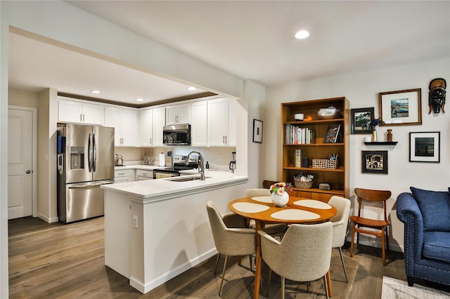 kitchen with appliances with stainless steel finishes, hardwood / wood-style floors, sink, kitchen peninsula, and white cabinetry