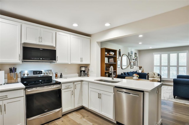 kitchen featuring white cabinetry, kitchen peninsula, stainless steel appliances, light hardwood / wood-style floors, and sink