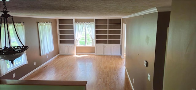 empty room with built in shelves, light hardwood / wood-style flooring, a textured ceiling, and ornamental molding