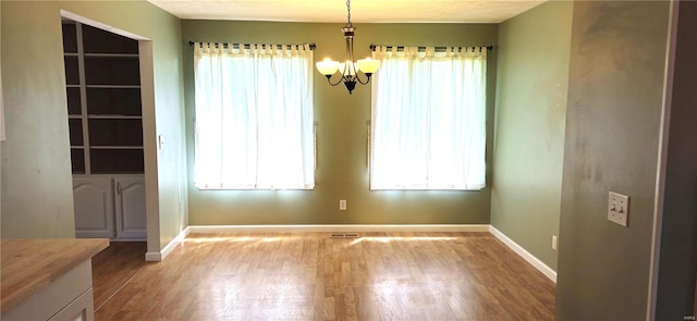 unfurnished dining area featuring a chandelier, a healthy amount of sunlight, and light hardwood / wood-style floors