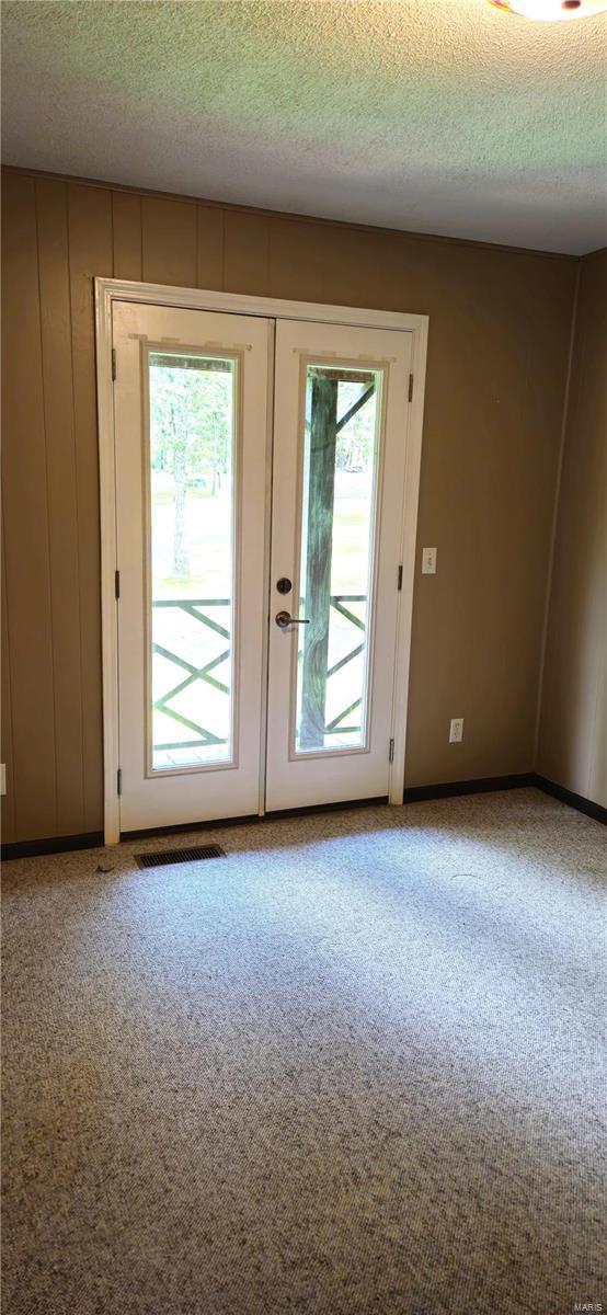 doorway featuring carpet flooring, wood walls, french doors, and a textured ceiling