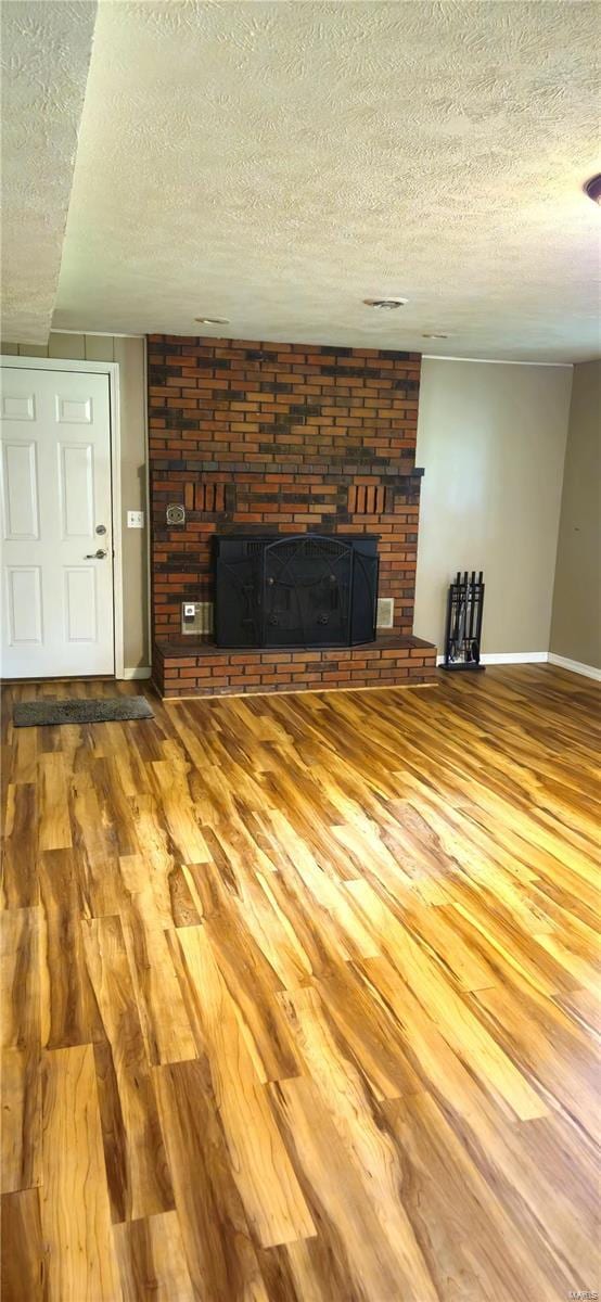 unfurnished living room with wood-type flooring, a large fireplace, and a textured ceiling