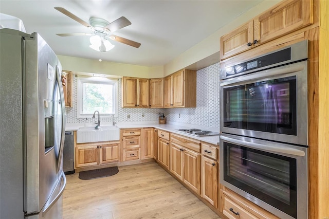 kitchen featuring light wood finished floors, stainless steel appliances, light countertops, decorative backsplash, and a sink