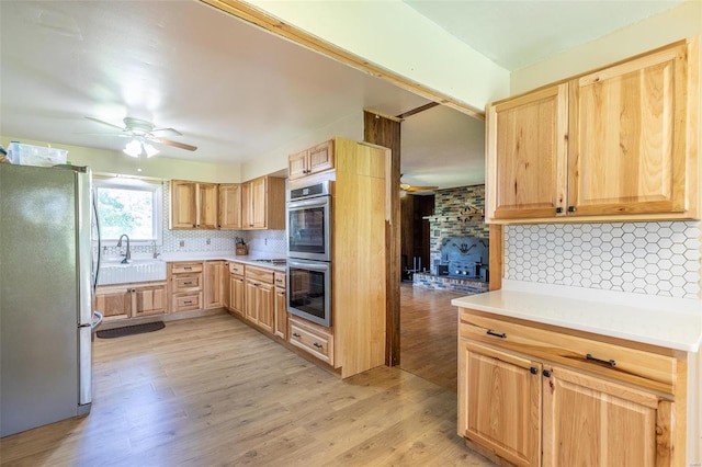 kitchen with appliances with stainless steel finishes, a sink, light brown cabinetry, light wood-style floors, and backsplash