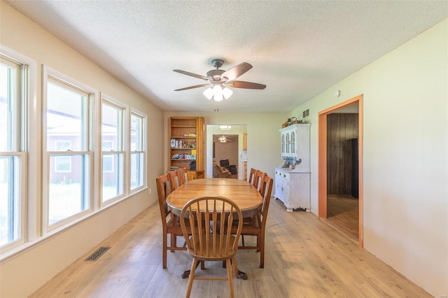 dining room with a textured ceiling, ceiling fan, light wood-type flooring, and visible vents