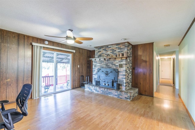 living area with a fireplace, a ceiling fan, wooden walls, a textured ceiling, and wood finished floors