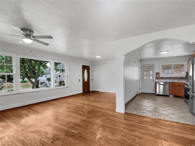 unfurnished living room featuring plenty of natural light, ceiling fan, light wood-type flooring, and ornamental molding