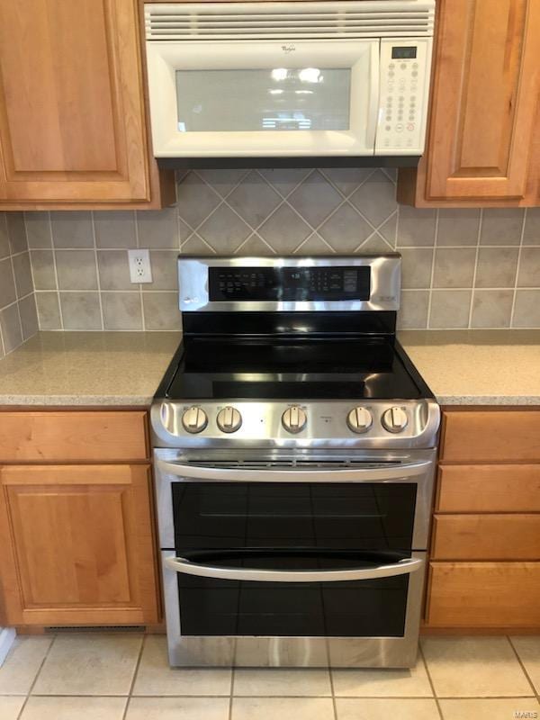 kitchen with light stone countertops, light tile patterned floors, decorative backsplash, and range with two ovens