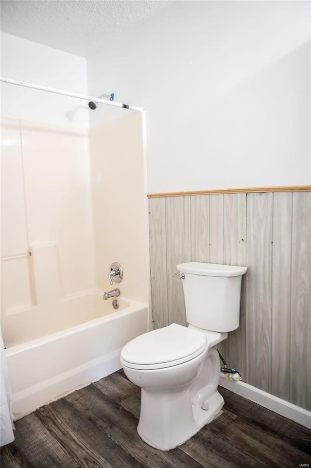 bathroom with a textured ceiling, toilet, shower / bathtub combination, and wood-type flooring