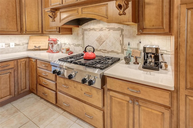 kitchen featuring stainless steel gas cooktop, backsplash, light tile patterned flooring, and custom range hood