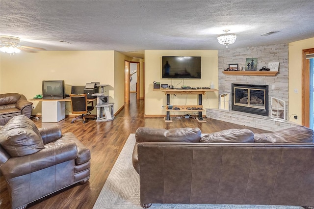 living room with hardwood / wood-style floors, a textured ceiling, a stone fireplace, and ceiling fan