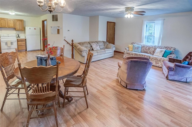 dining space with light hardwood / wood-style flooring, a textured ceiling, and ceiling fan with notable chandelier