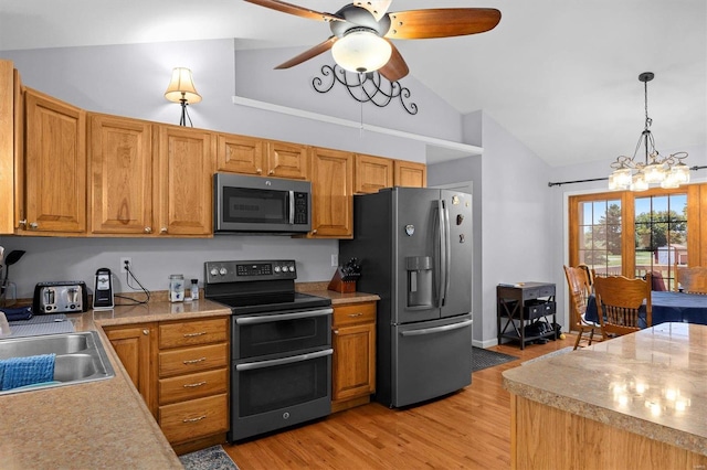 kitchen with vaulted ceiling, decorative light fixtures, sink, stainless steel appliances, and light wood-type flooring