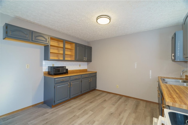 kitchen with decorative backsplash, a textured ceiling, sink, light hardwood / wood-style flooring, and butcher block countertops