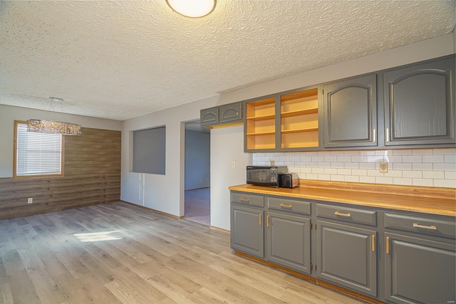 kitchen with pendant lighting, wood walls, wooden counters, decorative backsplash, and light hardwood / wood-style floors