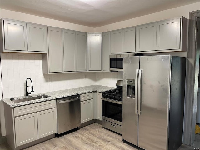 kitchen featuring light stone counters, light wood-type flooring, gray cabinetry, appliances with stainless steel finishes, and sink