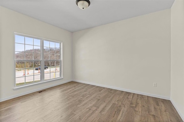 unfurnished room featuring baseboards, visible vents, and wood finished floors