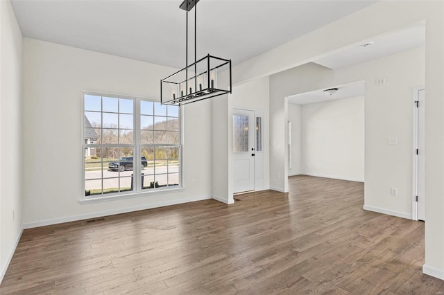 unfurnished dining area with a notable chandelier, baseboards, visible vents, and wood finished floors