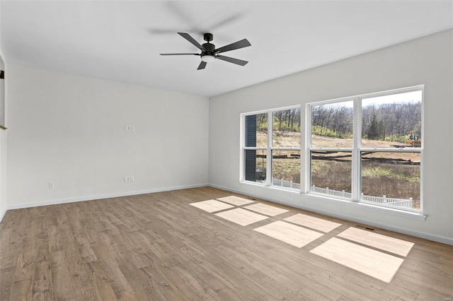 spare room featuring a ceiling fan, visible vents, baseboards, and wood finished floors