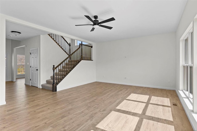 empty room featuring light wood-type flooring, plenty of natural light, stairway, and a ceiling fan