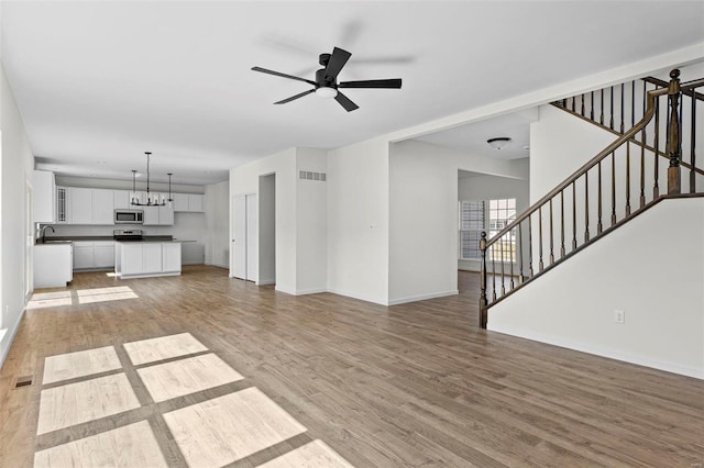 unfurnished living room with visible vents, stairway, and light wood-style flooring