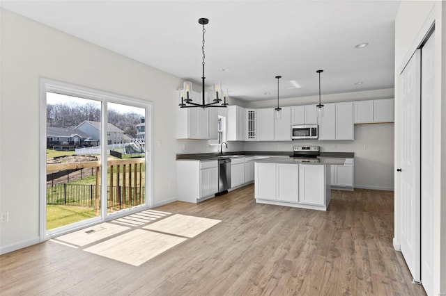 kitchen with light wood-style flooring, stainless steel appliances, a sink, white cabinets, and dark countertops