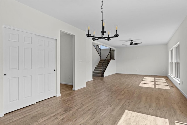 unfurnished living room featuring an inviting chandelier, baseboards, stairway, and wood finished floors