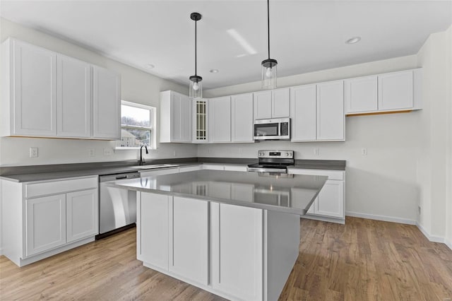 kitchen featuring stainless steel appliances, a kitchen island, a sink, white cabinets, and dark countertops