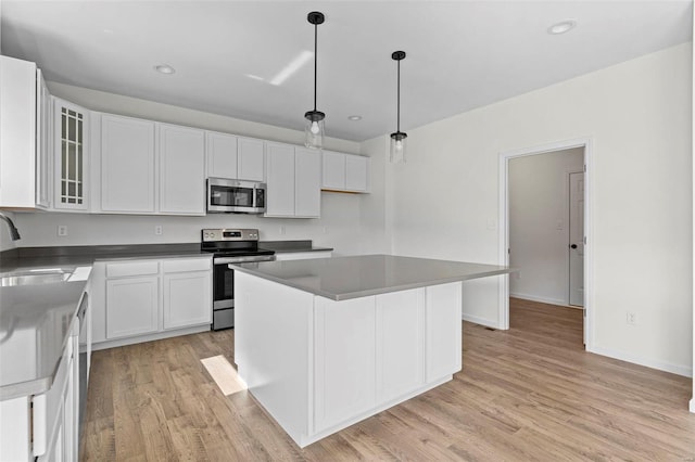 kitchen featuring a sink, light wood-style floors, white cabinets, appliances with stainless steel finishes, and glass insert cabinets