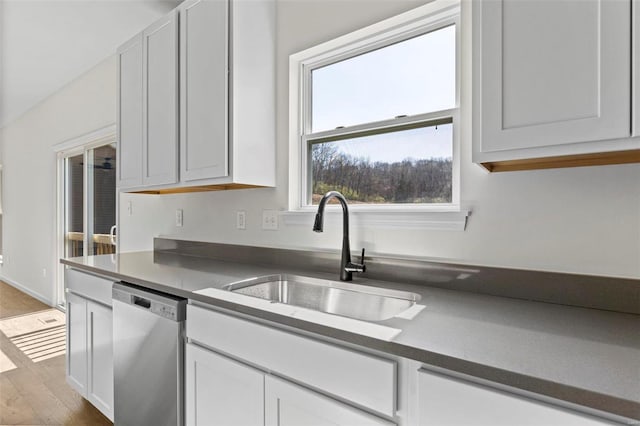 kitchen featuring white cabinets, dark countertops, wood finished floors, stainless steel dishwasher, and a sink