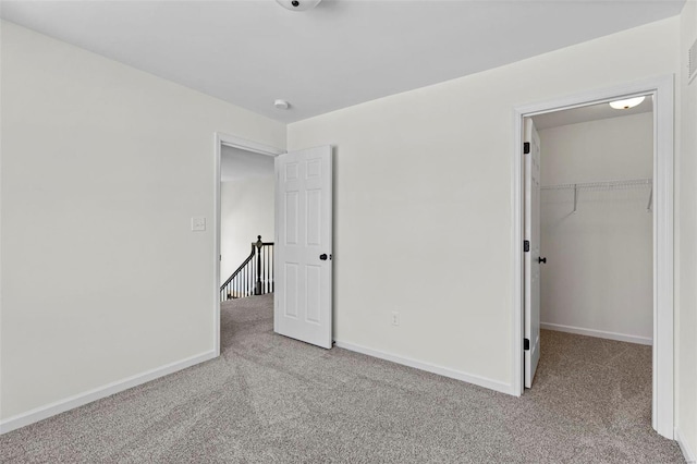 unfurnished bedroom with a closet, a spacious closet, baseboards, and carpet flooring