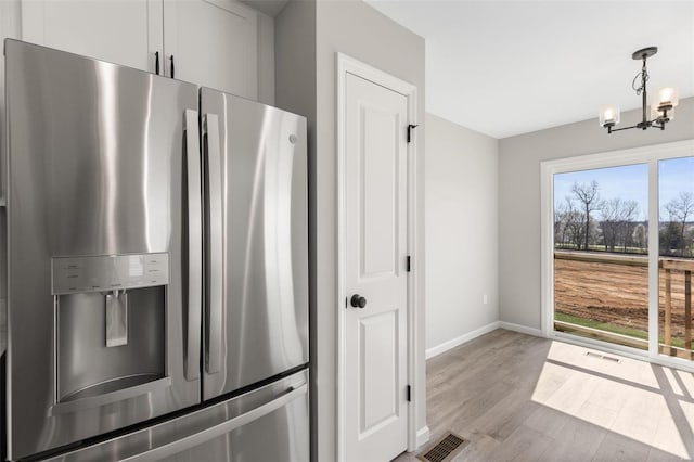 kitchen with hanging light fixtures, light wood-type flooring, a notable chandelier, stainless steel refrigerator with ice dispenser, and white cabinets