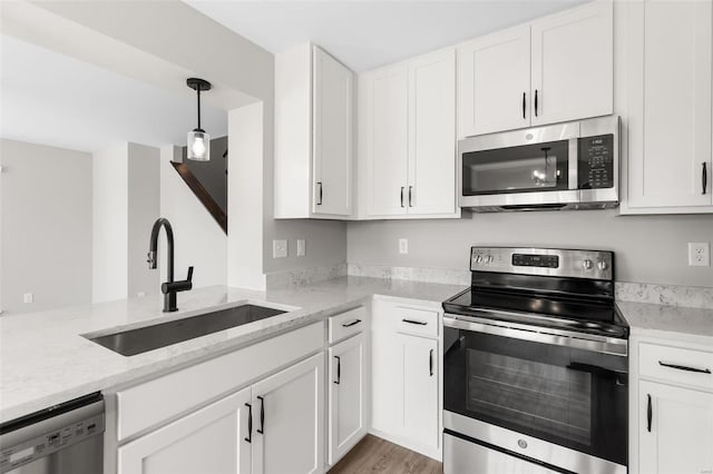 kitchen featuring appliances with stainless steel finishes, white cabinets, light stone countertops, and sink