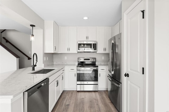 kitchen featuring kitchen peninsula, decorative light fixtures, stainless steel appliances, white cabinets, and sink