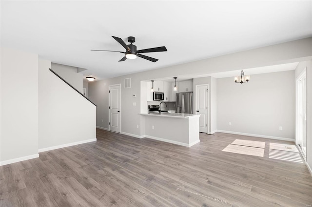 unfurnished living room with ceiling fan with notable chandelier, light hardwood / wood-style floors, and sink