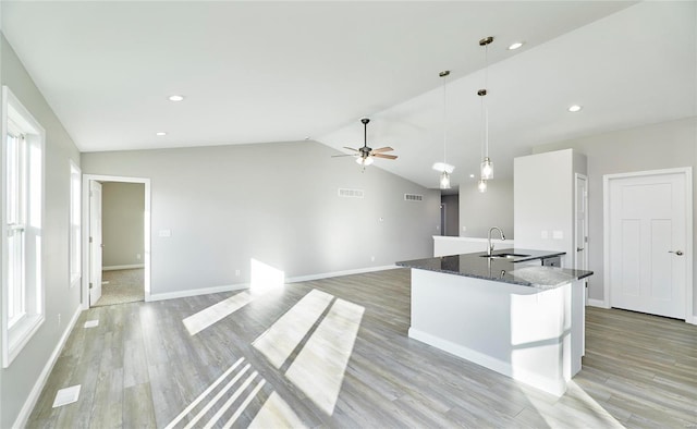 kitchen with sink, decorative light fixtures, vaulted ceiling, dark stone counters, and white cabinets