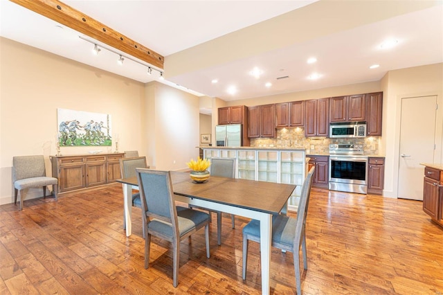 dining space with beam ceiling, light hardwood / wood-style floors, and rail lighting