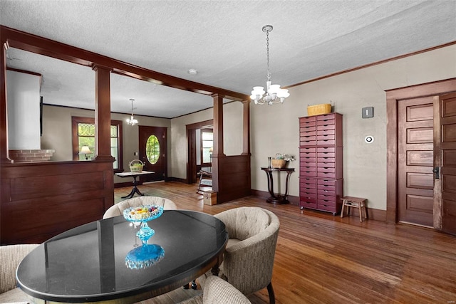 dining room featuring plenty of natural light, ornate columns, a textured ceiling, a notable chandelier, and dark hardwood / wood-style flooring