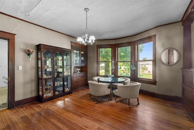 dining area with a chandelier, a textured ceiling, dark hardwood / wood-style flooring, and ornamental molding