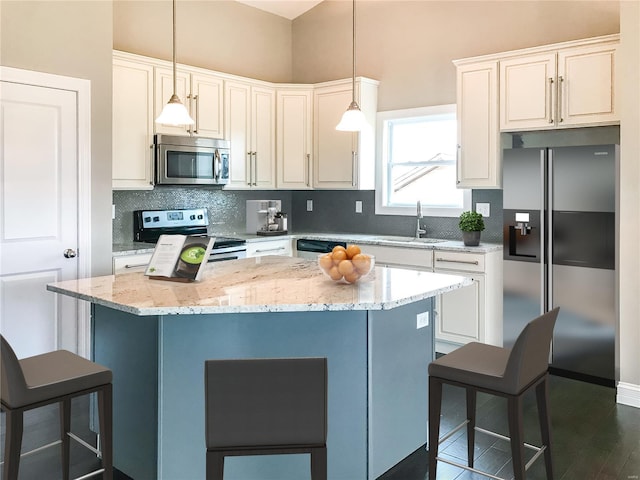 kitchen featuring appliances with stainless steel finishes, light stone counters, sink, a kitchen island, and hanging light fixtures