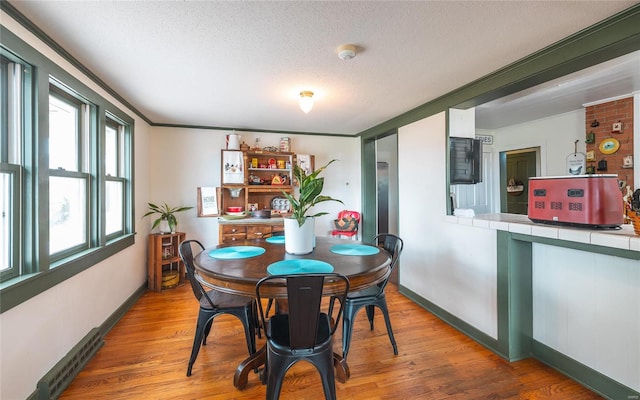 dining area with a textured ceiling, a wealth of natural light, brick wall, and hardwood / wood-style floors