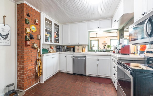 kitchen featuring tile counters, white cabinets, backsplash, stainless steel appliances, and ornamental molding