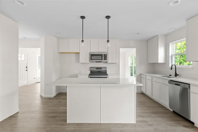 kitchen with sink, appliances with stainless steel finishes, decorative light fixtures, a kitchen island, and white cabinetry