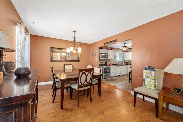 dining room featuring ceiling fan with notable chandelier, a textured ceiling, light hardwood / wood-style floors, and sink