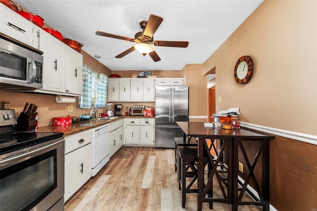 kitchen with sink, appliances with stainless steel finishes, a textured ceiling, white cabinets, and light wood-type flooring