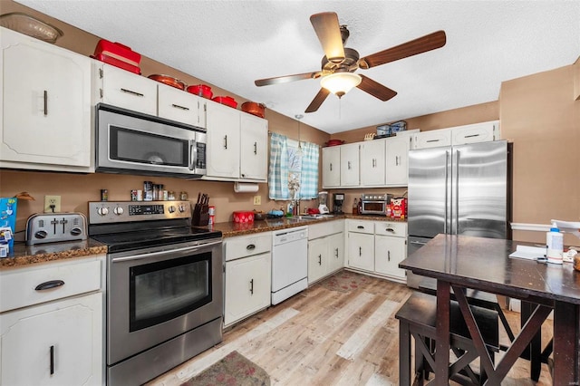 kitchen with white cabinets, light hardwood / wood-style floors, a textured ceiling, and appliances with stainless steel finishes