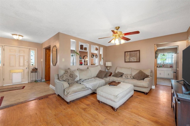 living room featuring ceiling fan, sink, light wood-type flooring, and a textured ceiling