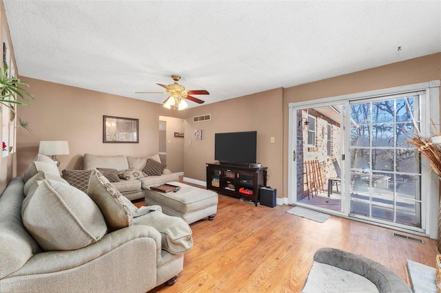 living room with ceiling fan, light wood-type flooring, and a textured ceiling